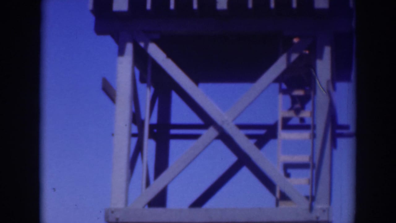 Worker on a ladder beside a raised tank and cross-braced tower supports.