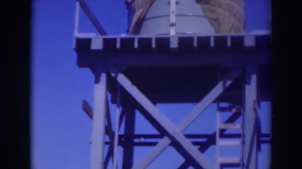 The Sacramento water-tower structure fills the frame, with a ladder, platform rail, tank surface, and braced wooden supports visible.