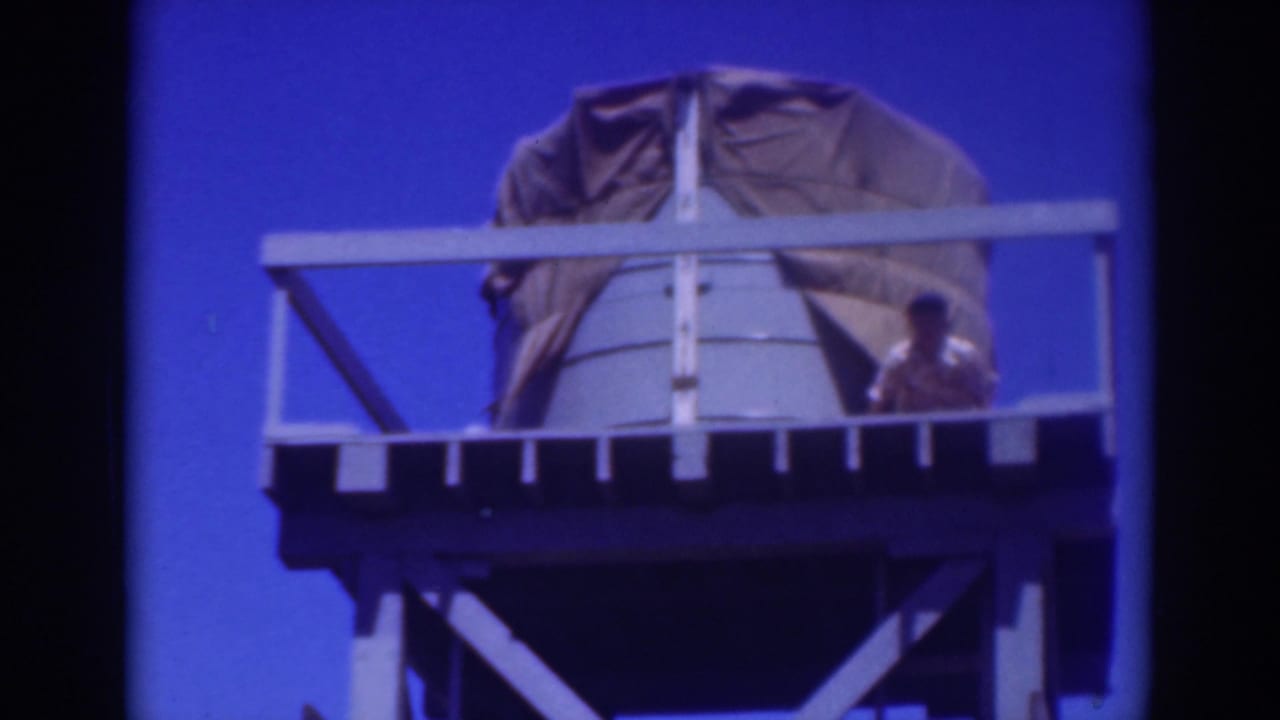Worker beside a covered water tank on an elevated platform against blue sky.