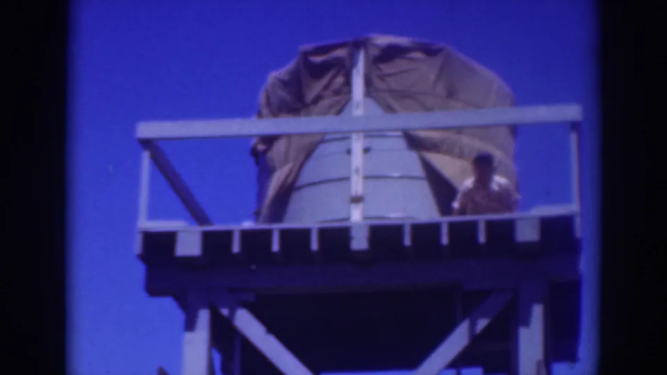 1937 Sacramento footage shows a worker near a tarp-covered water tank on a raised platform with pale railings.