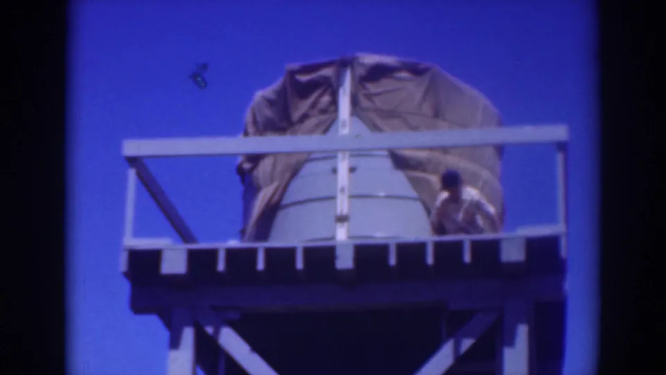 A worker in light clothing appears beside the right railing of a tarp-covered water tank in Sacramento, 1937.