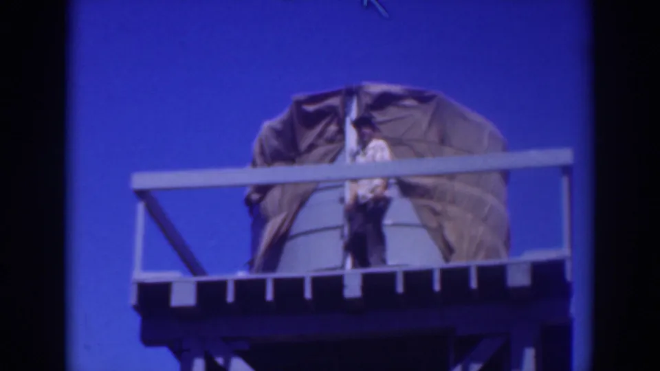 A worker stands upright on the Sacramento water tower platform next to the large tarp-covered tank.