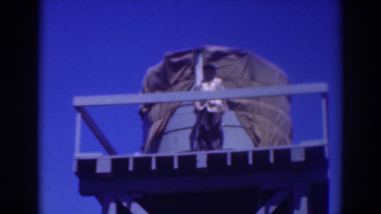 Person on a high platform beside a large covered object under a blue sky.