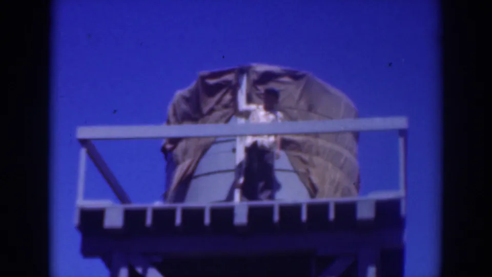 The final frame holds on the elevated platform, where a person in light clothing stands before the large draped object under the saturated sky.