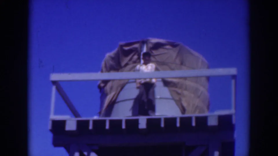 A 1937 Sacramento home-movie frame shows the man near the center of the platform, with the covered tank and railings visible around him.