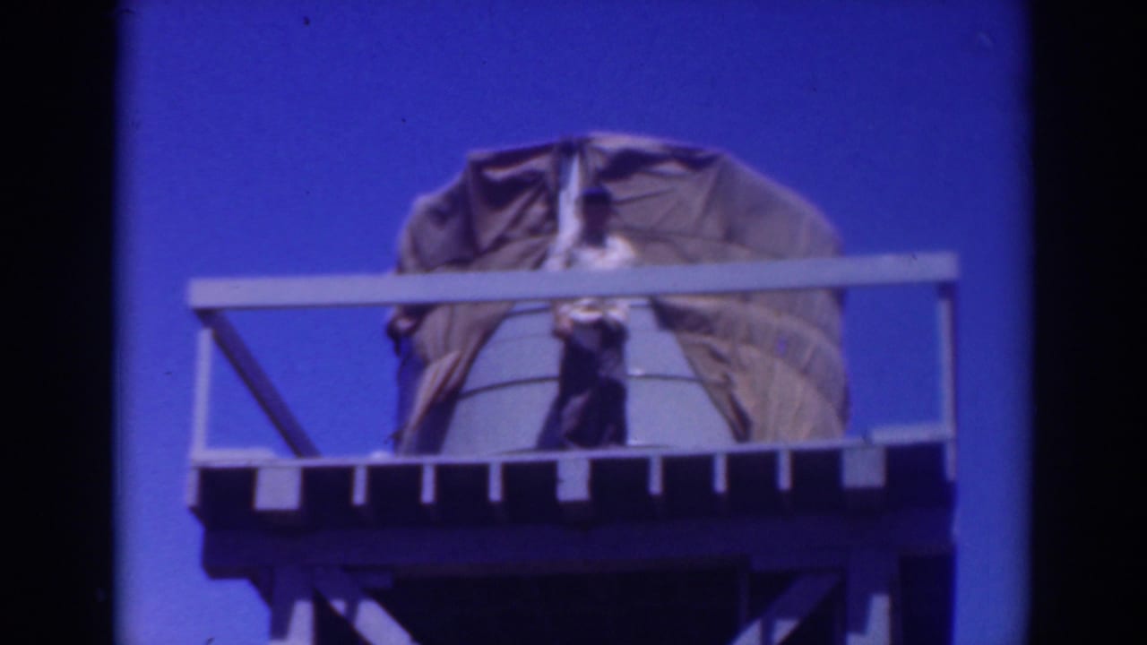 Man remains on the platform in front of a large covered tank and white railings.