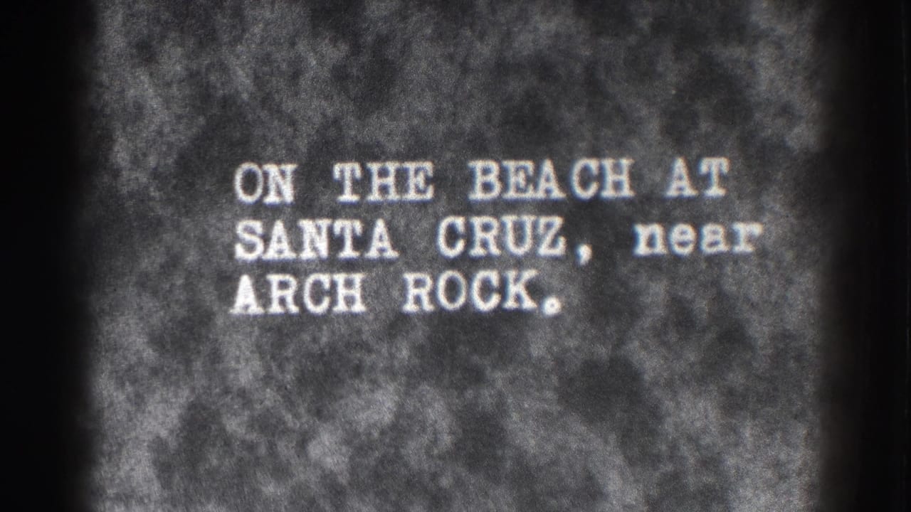 Typed title card reading on the beach at Santa Cruz near Arch Rock.