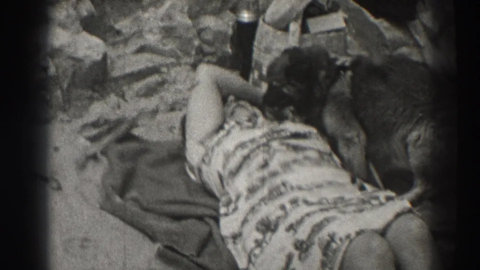 1937 Santa Cruz home-movie frame showing a woman lying on a beach towel beside a family dog on the sand.