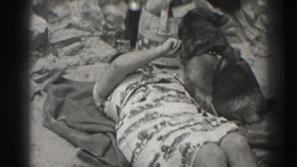 A woman lies on a Santa Cruz beach blanket and reaches toward a small dog beside her in the 1937 home-movie frame.