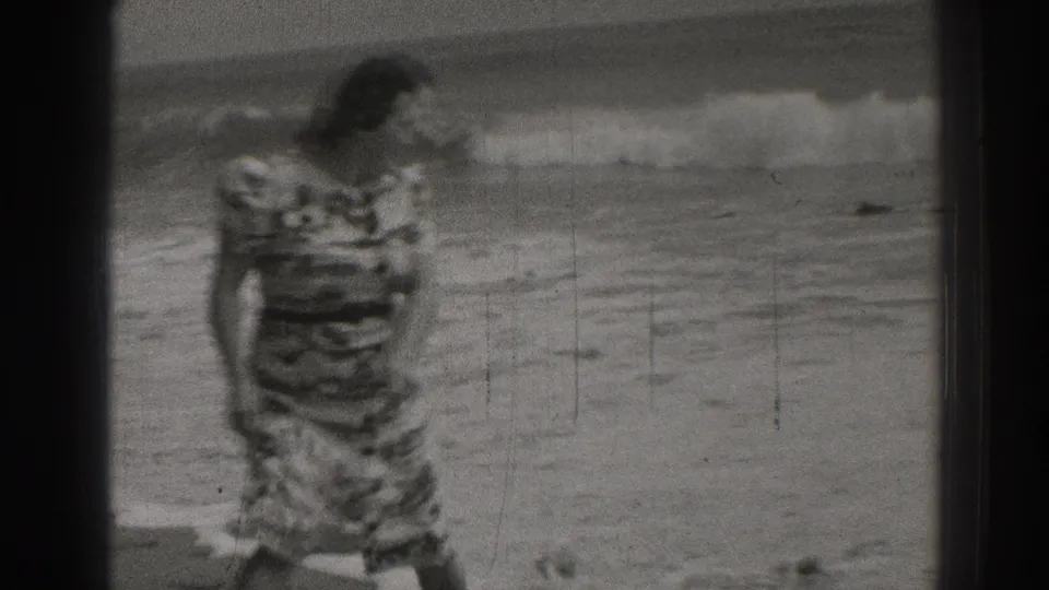 A closer 8mm frame shows the woman in a patterned dress on the beach, with soft focus and surf visible in the background.