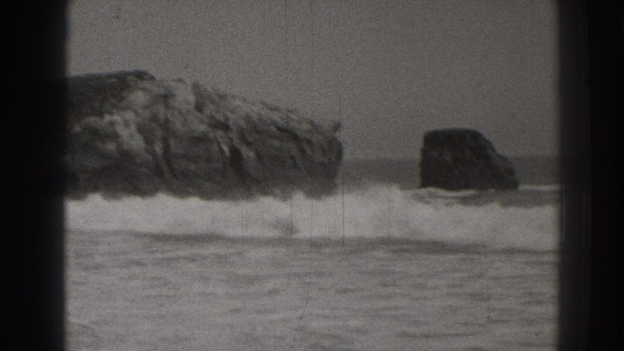 1937 Santa Cruz coastal home-movie frame showing two offshore rocks with surf breaking below an overcast sky.