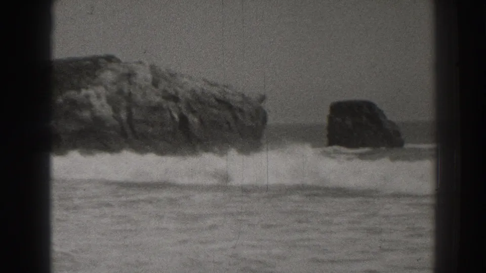 1937 Santa Cruz coastal home-movie frame showing two offshore rocks with surf breaking below an overcast sky.