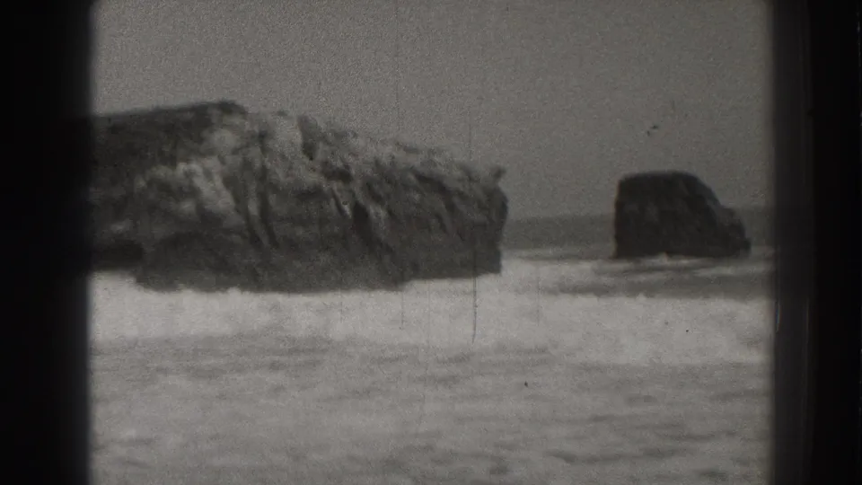 Black-and-white 8mm frame of Santa Cruz sea stacks with foamy waves moving across the foreground.
