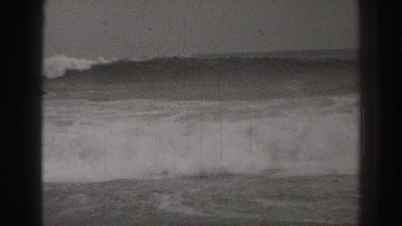 Large waves breaking across open water, seen through dark frame-edge shadows.