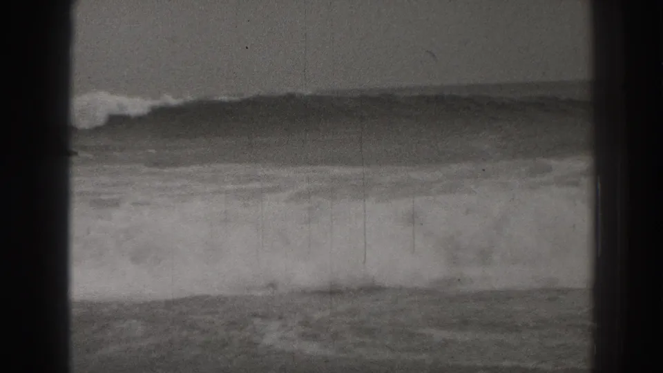 1937 Santa Cruz 8mm frame showing rough surf and foamy waves under a hazy horizon, partially bordered by dark film-gate shadows.