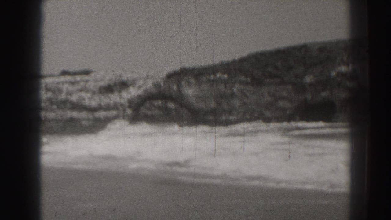 1937 Santa Cruz coastal footage showing surf breaking against a jagged rock formation in a grainy black-and-white frame.
