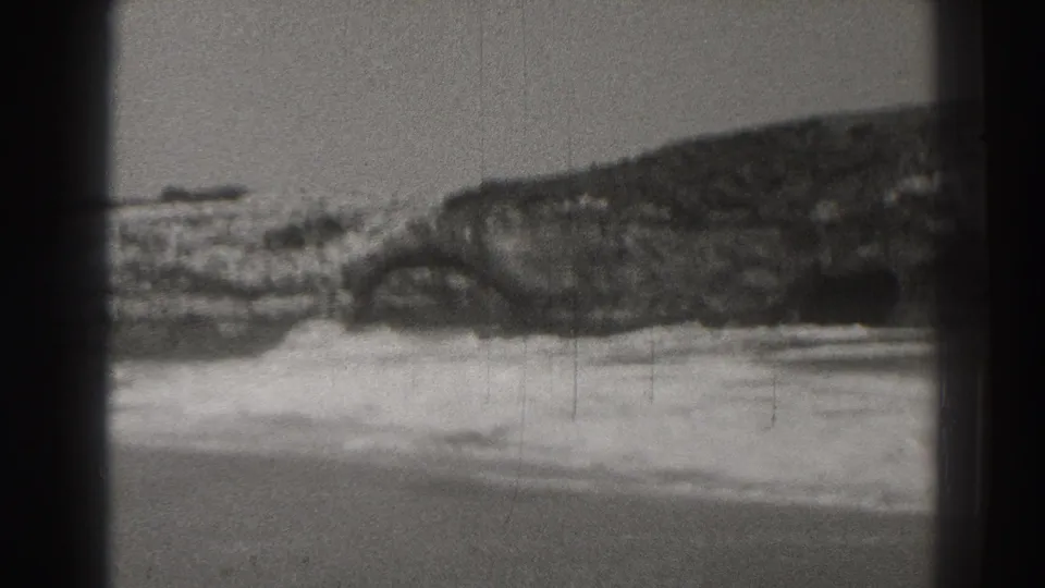 1937 Santa Cruz coastal footage showing surf breaking against a jagged rock formation in a grainy black-and-white frame.