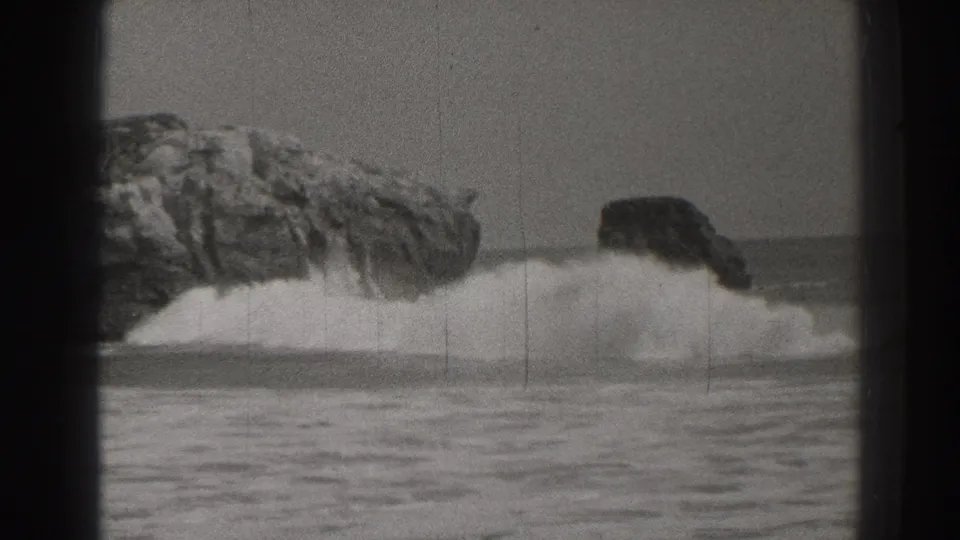1937 black-and-white home-movie view of a wave breaking against a rocky Santa Cruz shore, with open water in front.