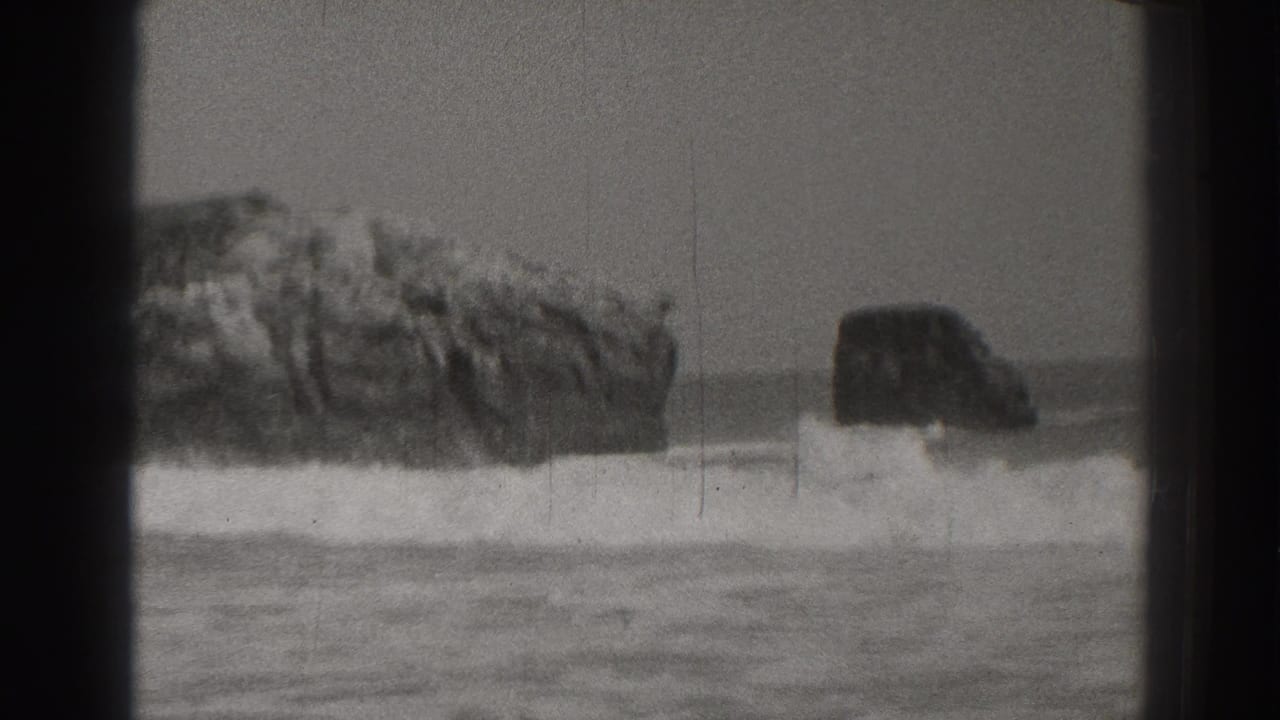 Surf breaks against dark coastal rocks beside a sandy beach.