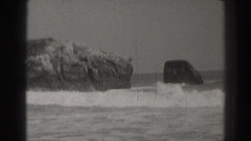 1937 Santa Cruz home-movie frame showing ocean waves striking rugged rocks near a sandy beach.