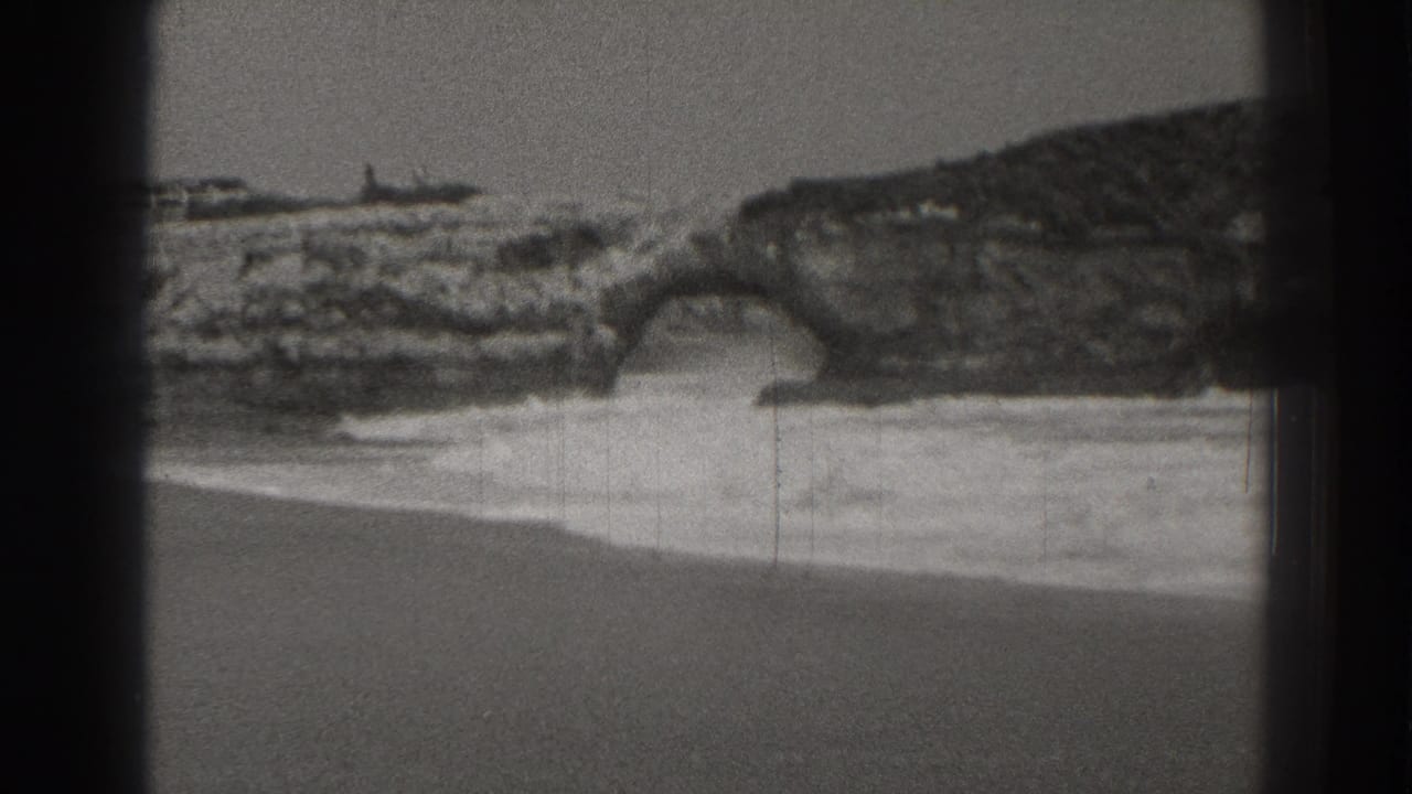 Rocky shoreline with a natural arch and surf rolling below.