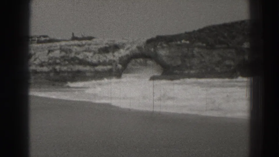 Santa Cruz coastal rocks and a natural sea arch appear above breaking surf in this 1937 8mm frame.