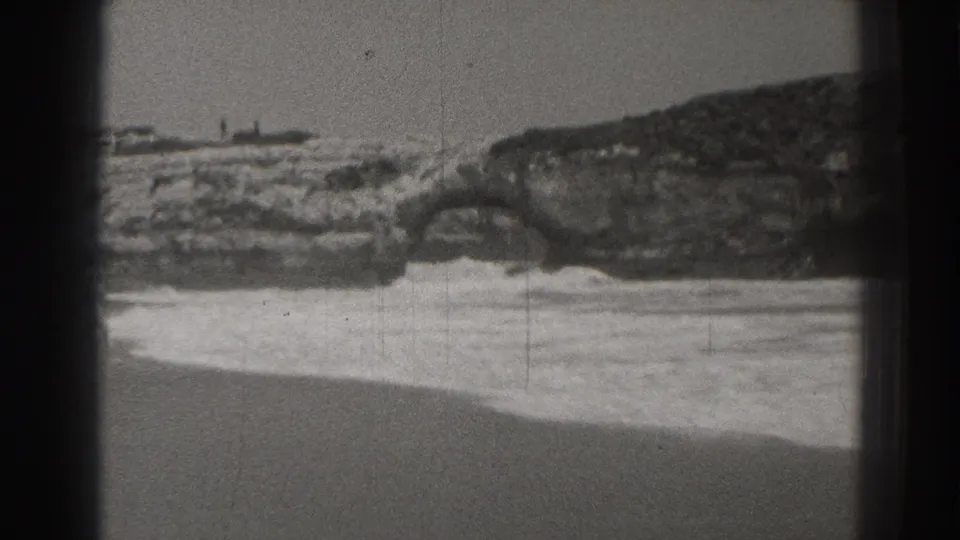 1937 Santa Cruz shoreline view with sandy beach, foamy surf, and a rock arch in the background.