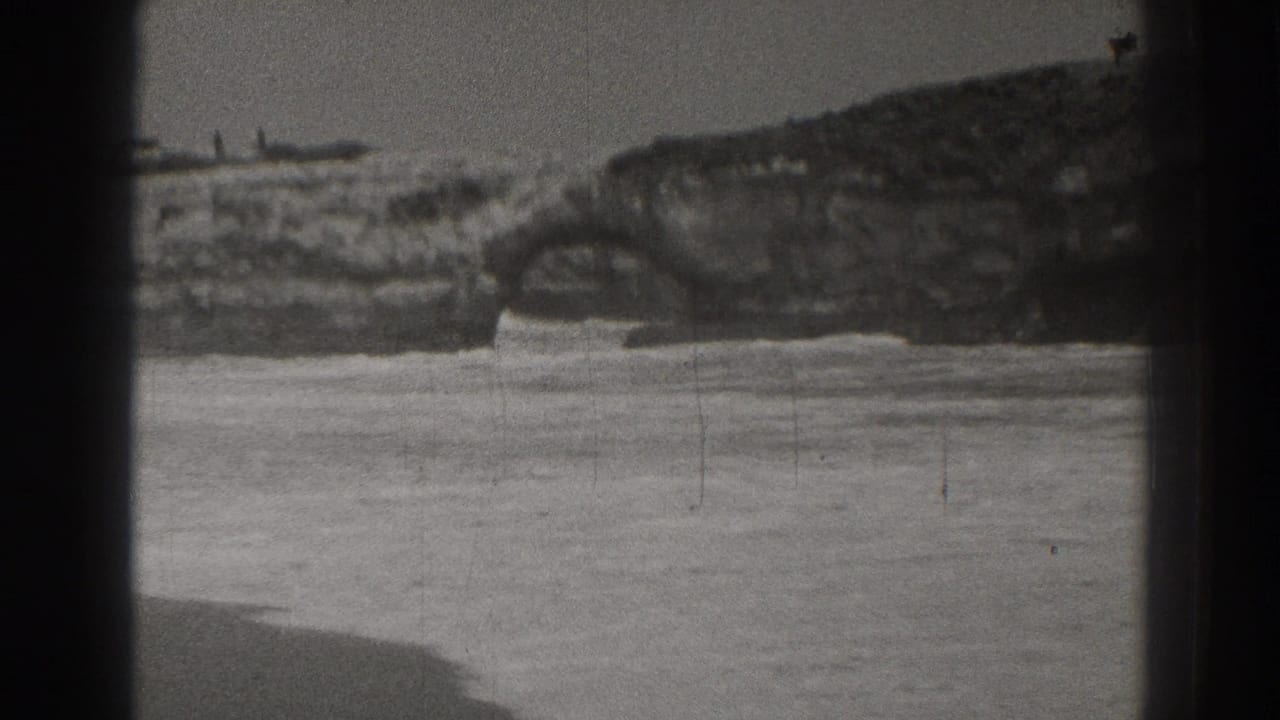 1937 Santa Cruz coastal home-movie frame showing rocky shore and water with heavy gate shadowing and film grain.