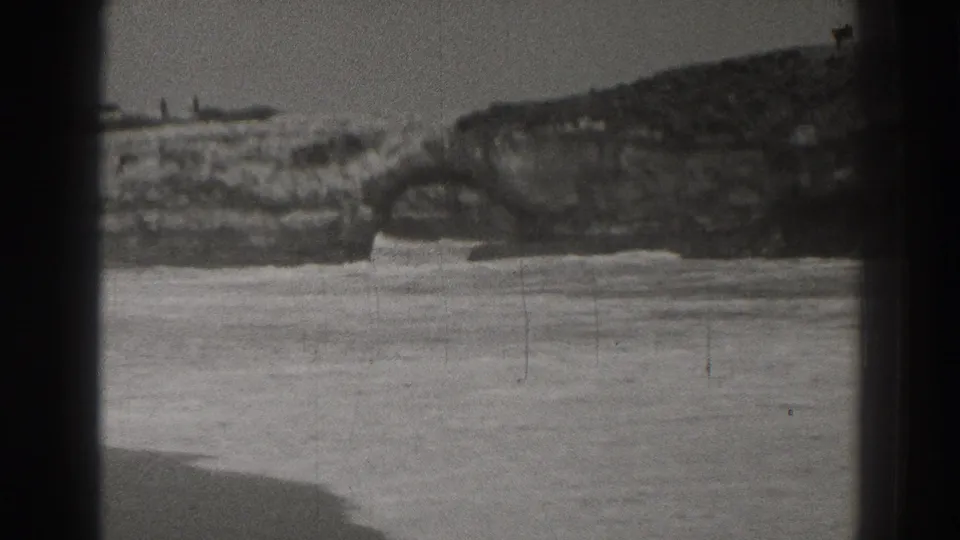 1937 Santa Cruz coastal home-movie frame showing rocky shore and water with heavy gate shadowing and film grain.