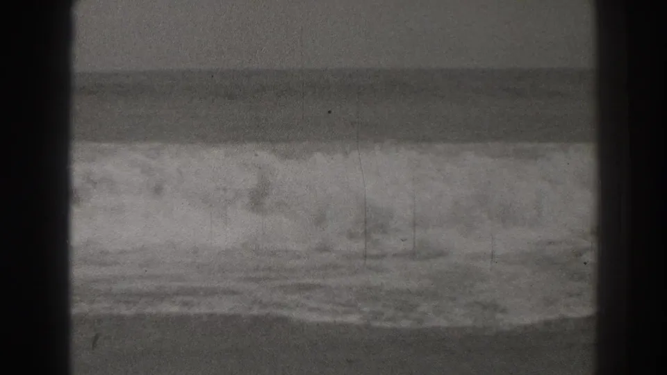 Santa Cruz surf breaks in a soft black-and-white 8mm frame, with grain, scratches, and a low horizon visible.
