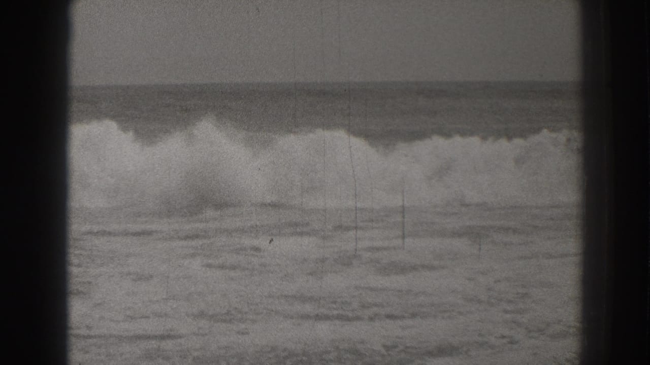 1937 Santa Cruz 8mm frame showing a broad surf break with foam rolling toward the beach.