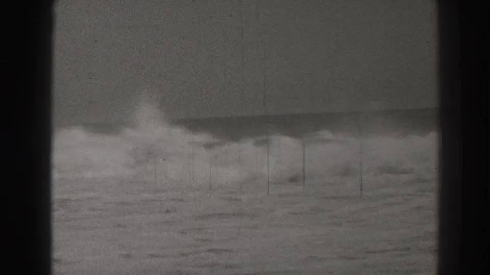 Black-and-white home-movie frame of Santa Cruz surf, with foamy water below a soft, hazy horizon.