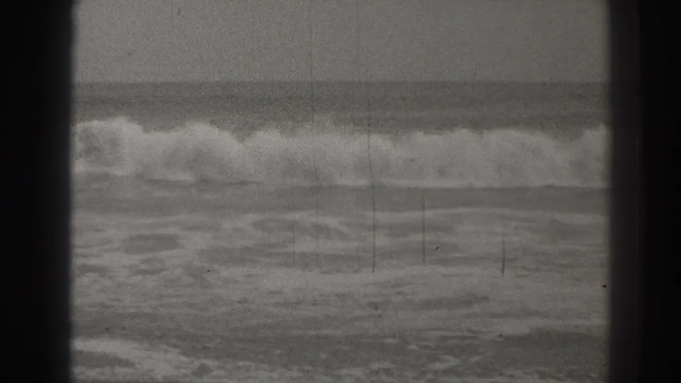 A breaking Santa Cruz wave fills the middle distance, framed by dark edges and marked by visible 8mm grain and scratches.