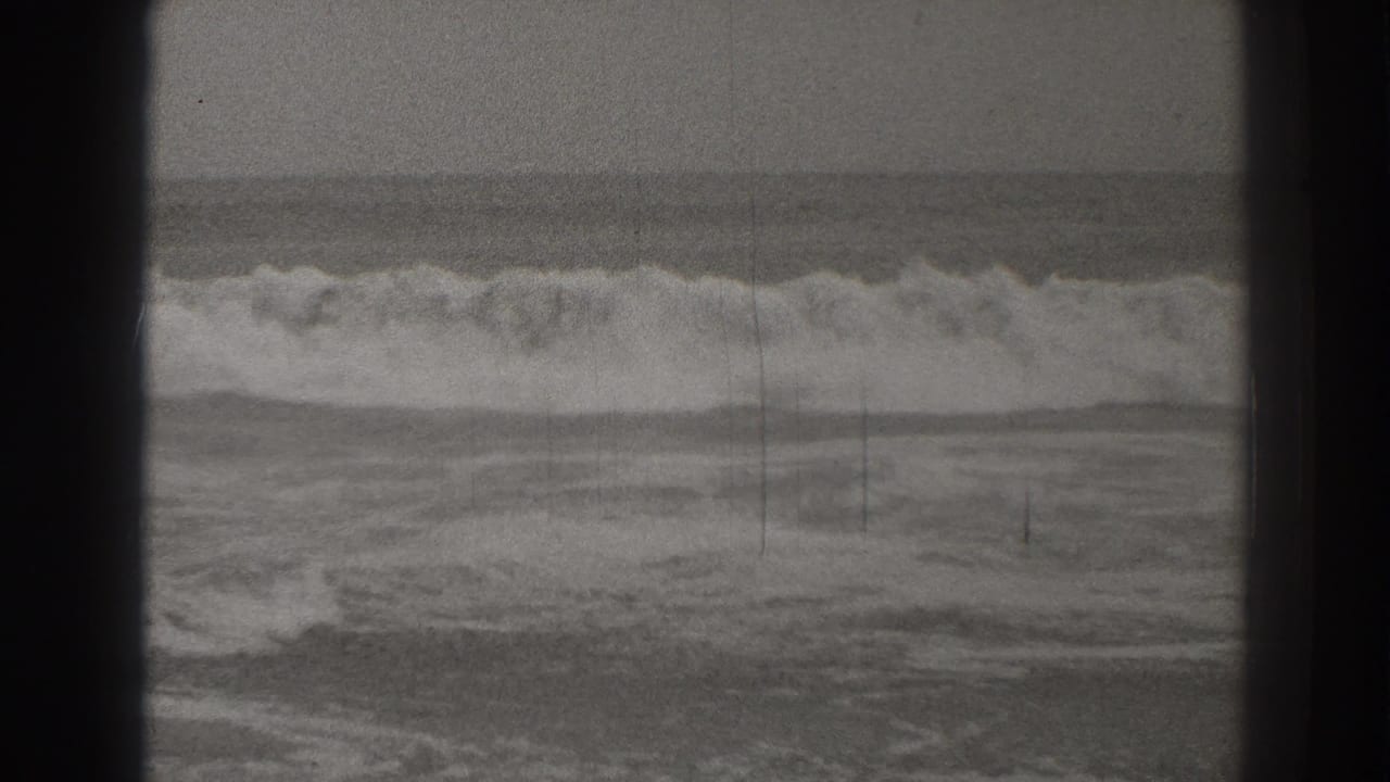 Foamy ocean waves breaking near shore behind dark film frame borders.