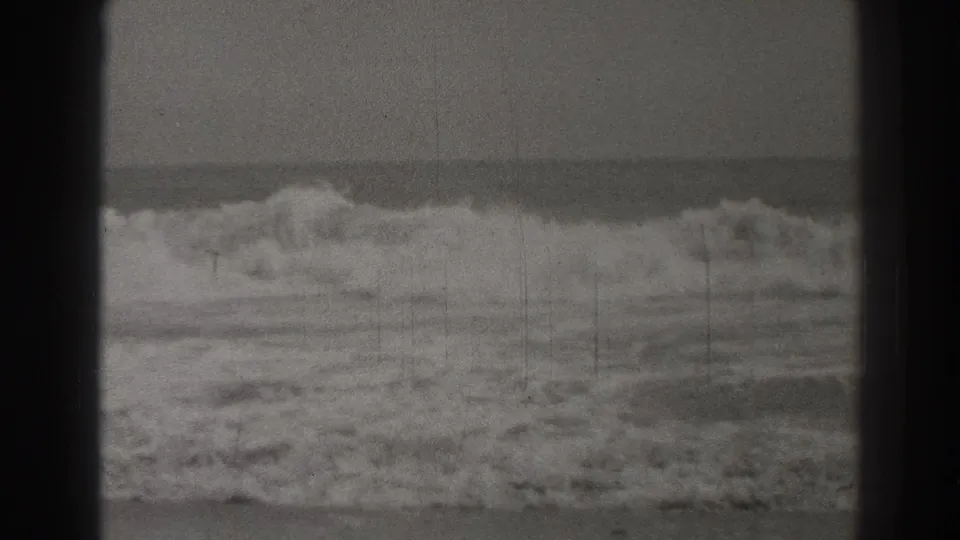 1937 Santa Cruz 8mm frame showing rough surf rolling toward shore beneath an overcast sky, with visible grain and dark gate borders.