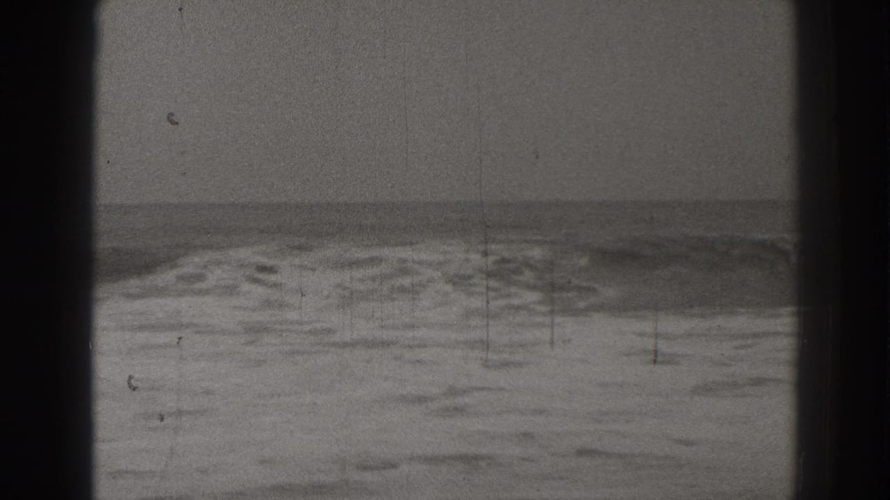 Breaking surf beneath a flat ocean horizon with dark film borders.