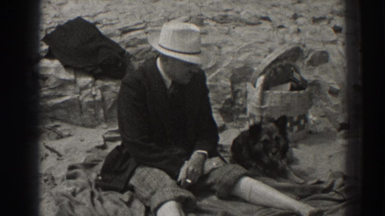 1937 Santa Cruz home-movie frame showing a seated man in a light fedora beside a dark dog on rocky ground.
