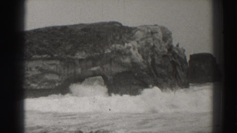 Santa Cruz coastal rock arch fills the frame as foamy surf spreads across the lower edge in grainy 1937 8mm footage.