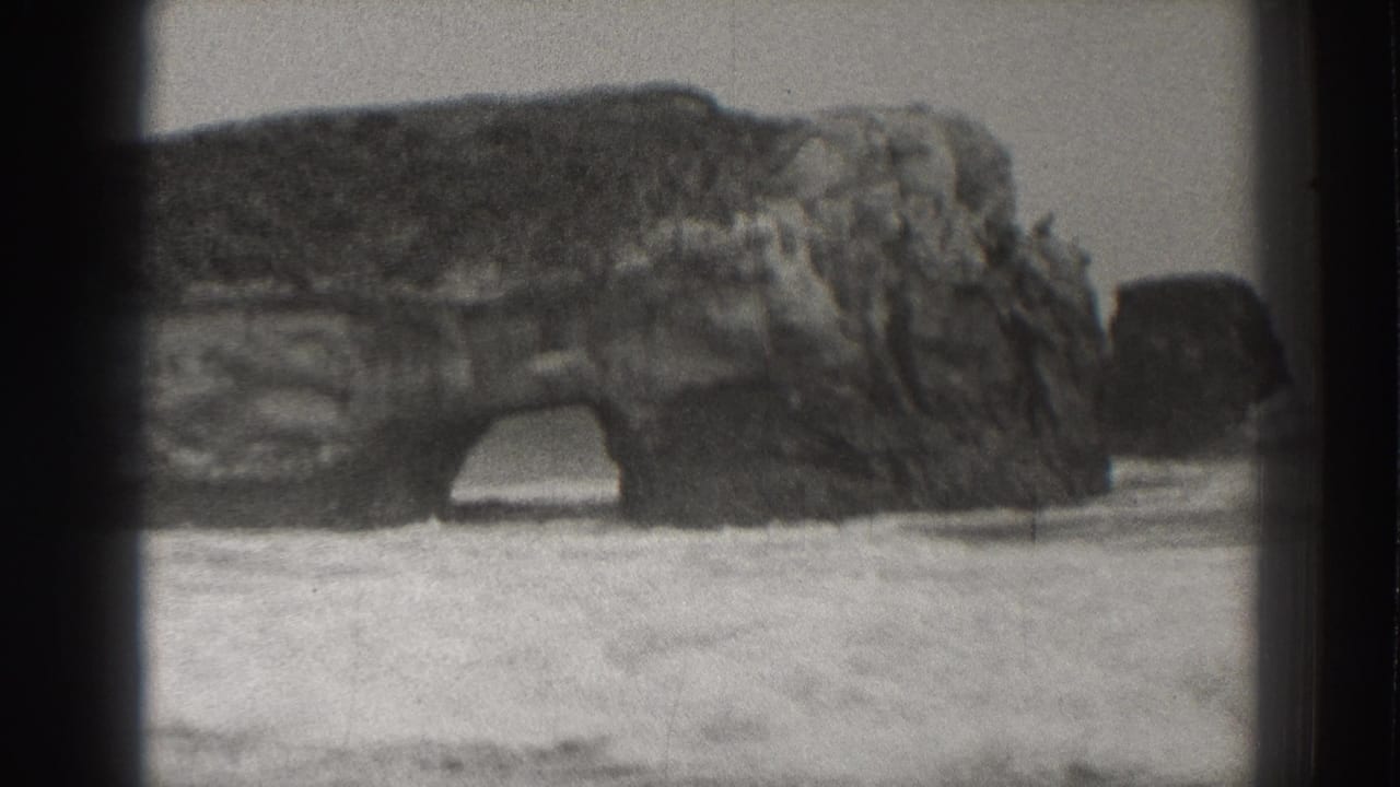 Rocky sea arch with surf and foam washing across the foreground beach.