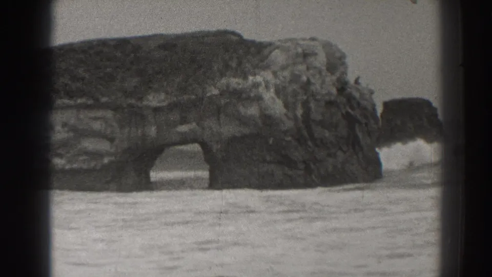 1937 Santa Cruz beach footage showing a sea arch, nearby rock stack, and white foam traveling across wet sand.
