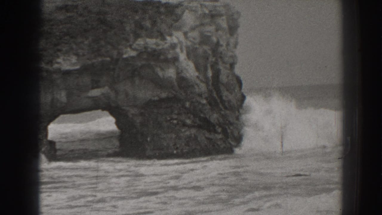 1937 Santa Cruz 8mm frame showing waves pushing through a rugged coastal sea arch in black and white.