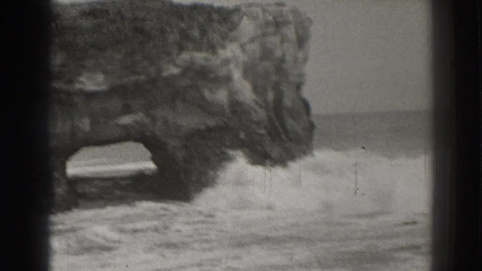 Black-and-white 8mm view of surf splashing against a Santa Cruz coastal rock arch in 1937.