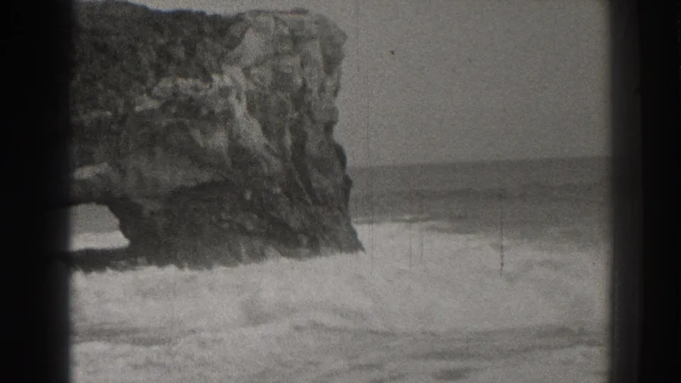 1937 Santa Cruz home-movie frame with foaming waves below a rugged natural sea arch.