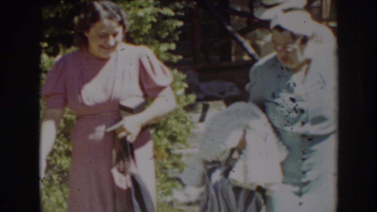 Two women outdoors in dresses and hats near greenery, one holding a purse and pale garment.