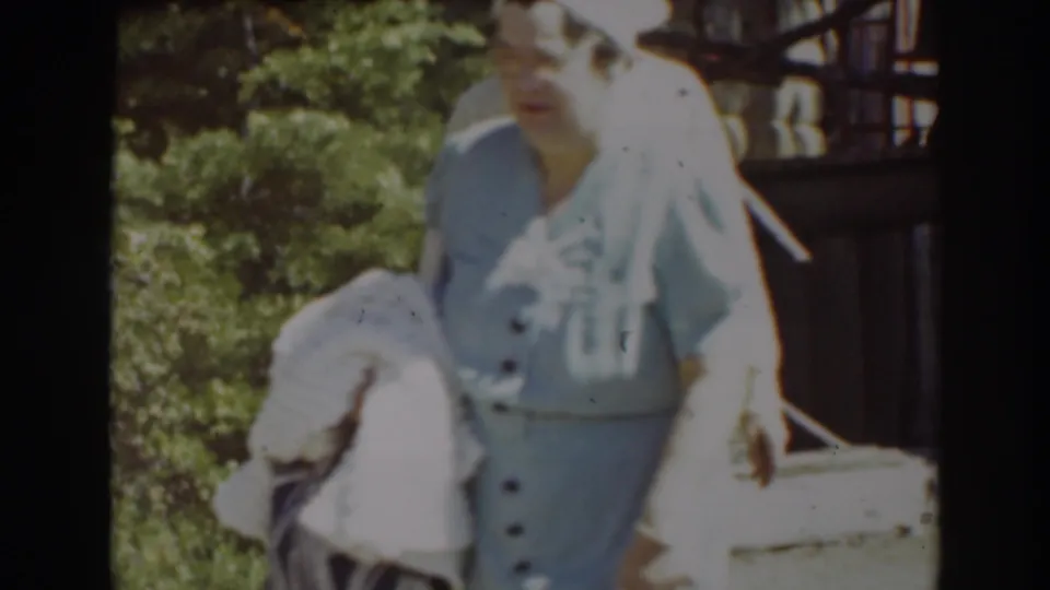 A woman in a light blue outfit and white hat stands outdoors in Truckee, holding a pale garment as the home-movie frame catches bright sunlight.