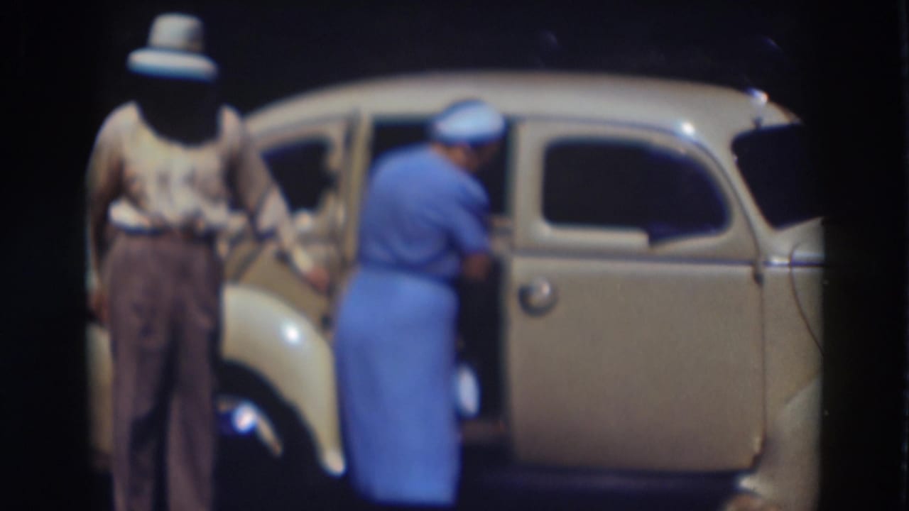 In the Truckee 1937 home-movie scene, the man stands at the rear door while the woman in blue begins to move toward the back seat.