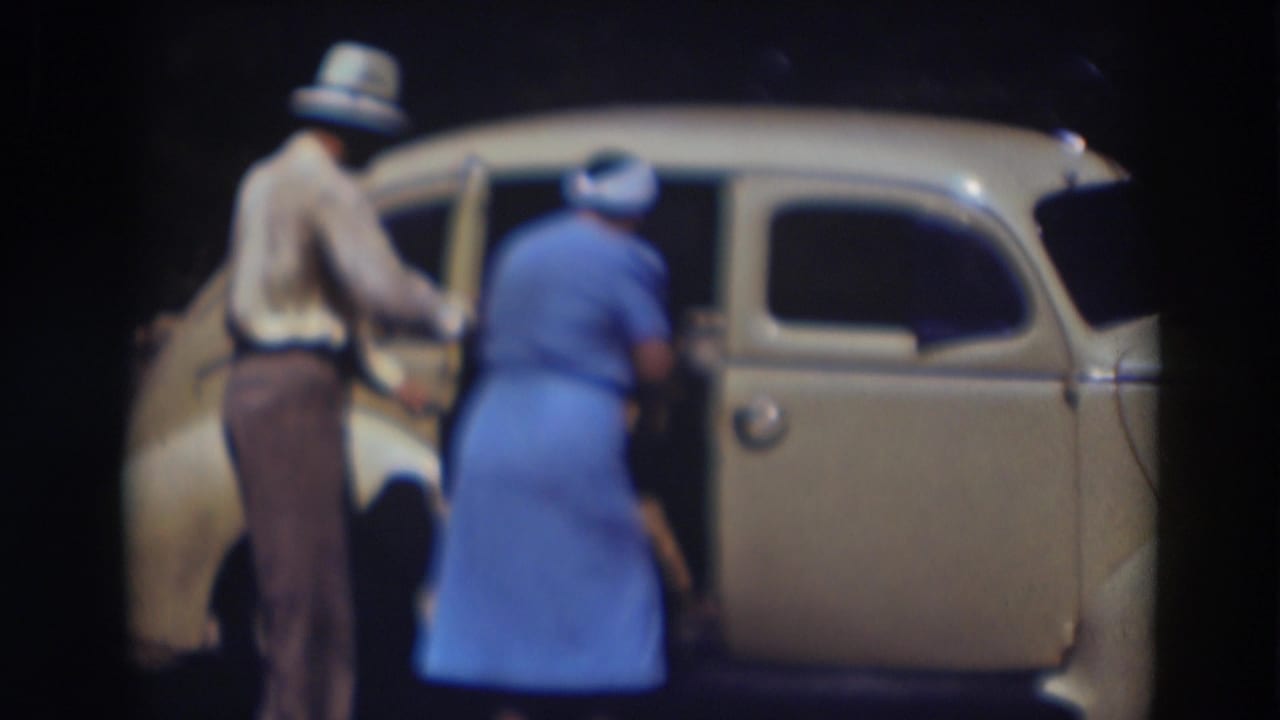 The woman in blue bends toward the back seat of the cream sedan in Truckee, with the man close by at the open rear door.