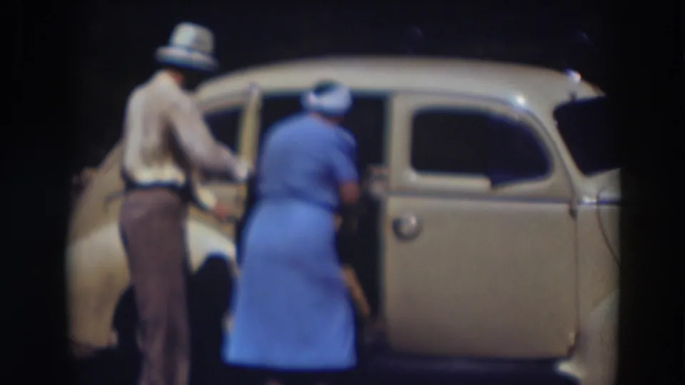 The woman in blue bends toward the back seat of the cream sedan in Truckee, with the man close by at the open rear door.