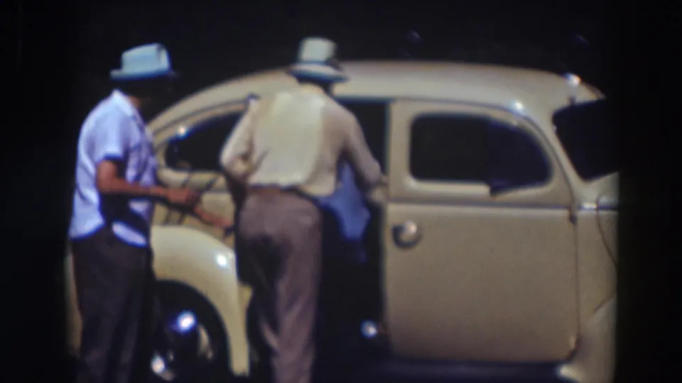 In 1937 Truckee, California footage, two adult men stand by a cream-colored car as a passenger begins entering the rear seat.
