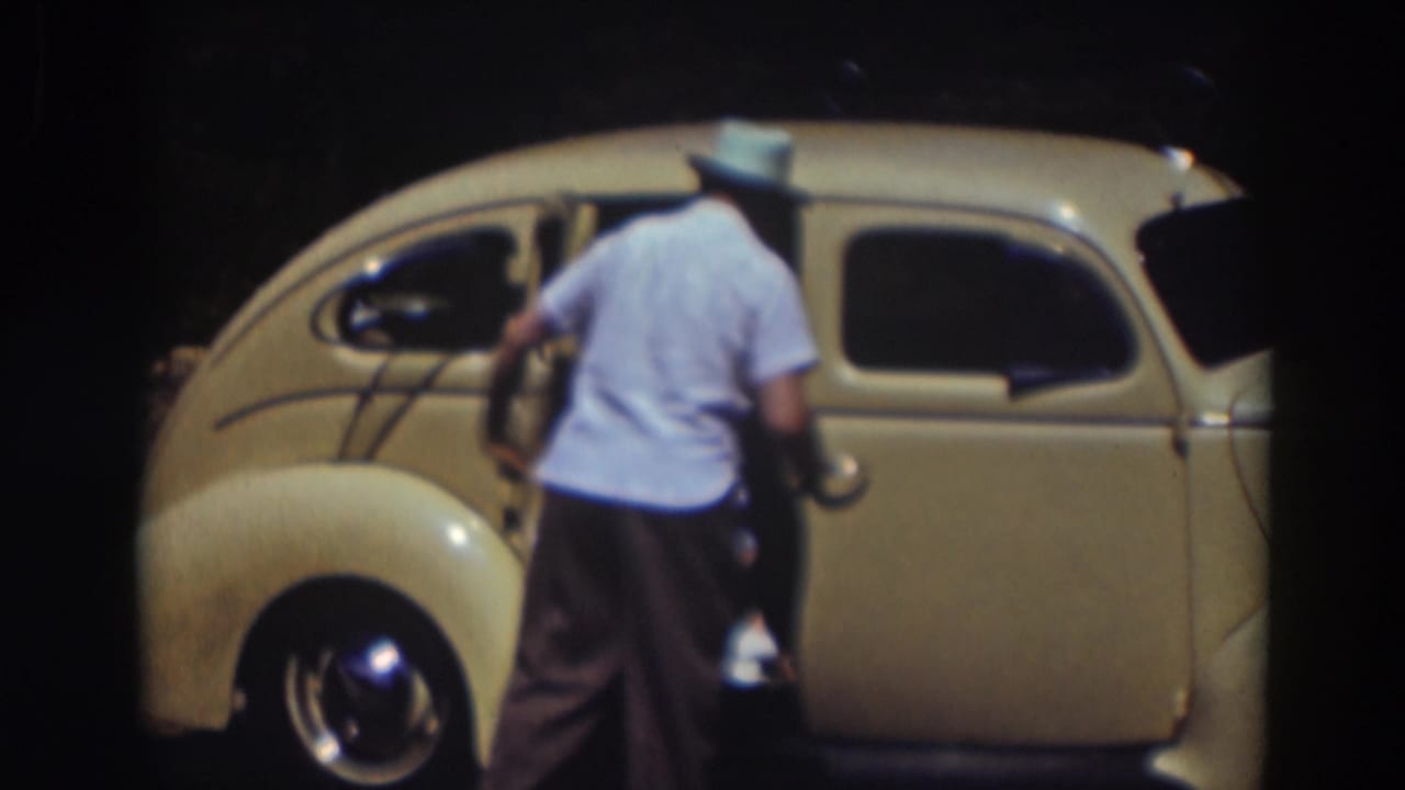 Two men stand beside a pale yellow compact car with one door open.